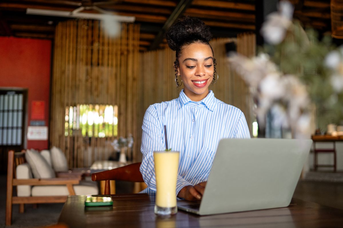 Freelance heureuse dégustant un petit-déjeuner nutritif composé d'un smoothie et d'une salade tout en travaillant sur un ordinateur portable.