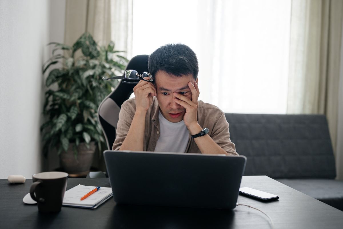Homme fatigué portant des lunettes travaillant à la maison avec un ordinateur portable.
