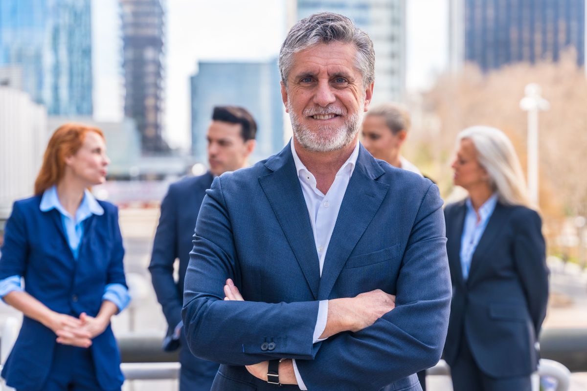 Le portage salarial après 50 ans Un homme d’affaires en costume professionnel se tient devant un groupe de professionnels